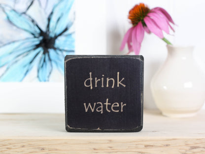 Small distressed black block sign with the words "drink water".