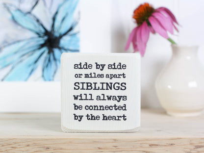 Small wood block with sister quote in whitewash that reads "Side by side or miles apart siblings will always be connected by the heart."