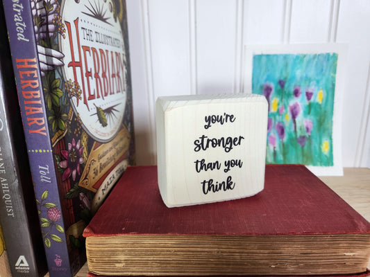 Decorative block with motivational quote on a stack of books with a painting in the background
