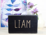 Freestanding small wood sign in distressed black with the name Liam in a fun upper case font