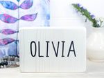 Freestanding small wood sign in whitewash with the name Olivia in a fun upper case font