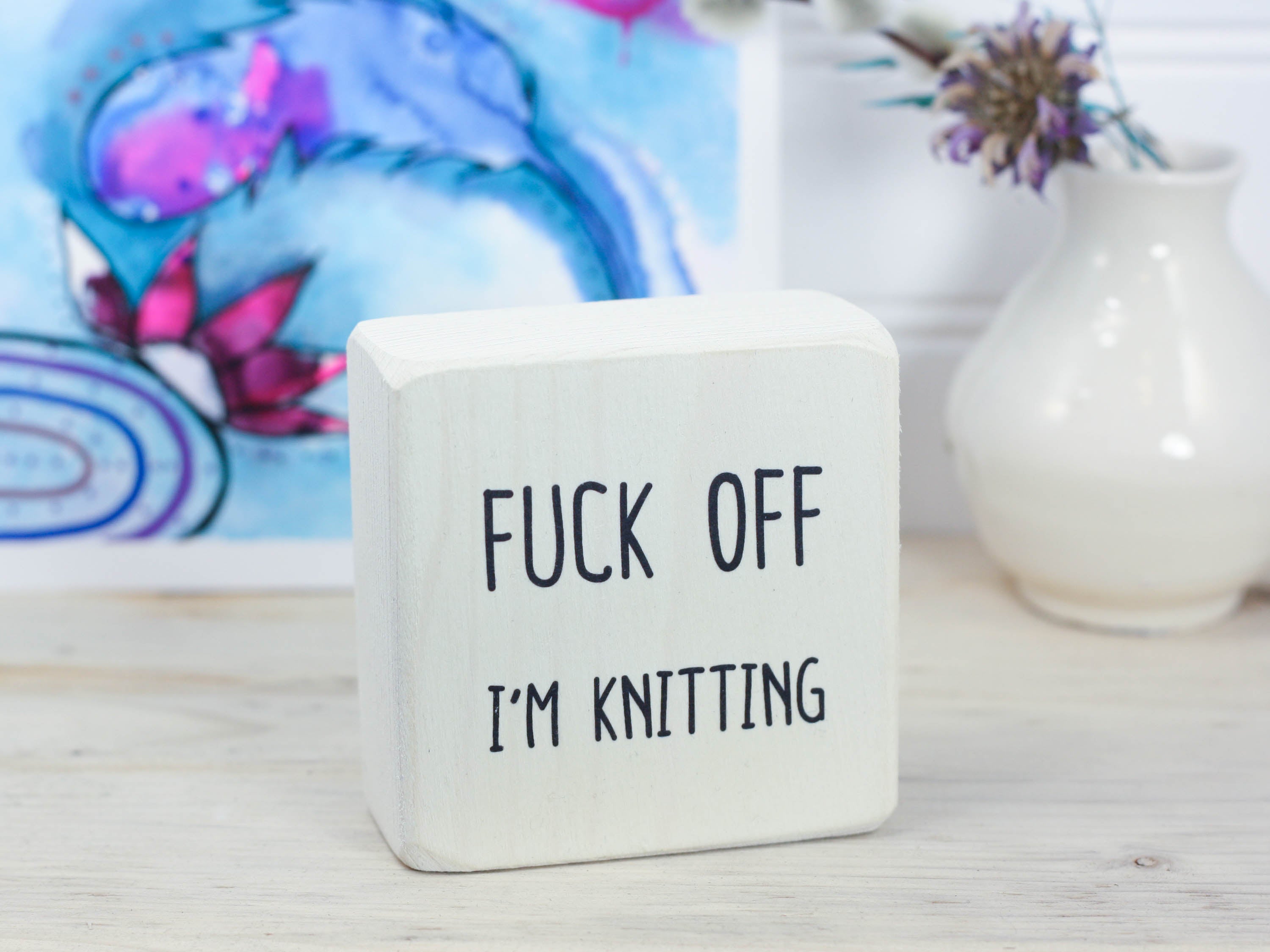 Small whitewashed wood sign with the saying "fuck off I'm knitting"