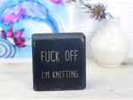 Small distressed black wood sign with the saying "fuck off I'm knitting"
