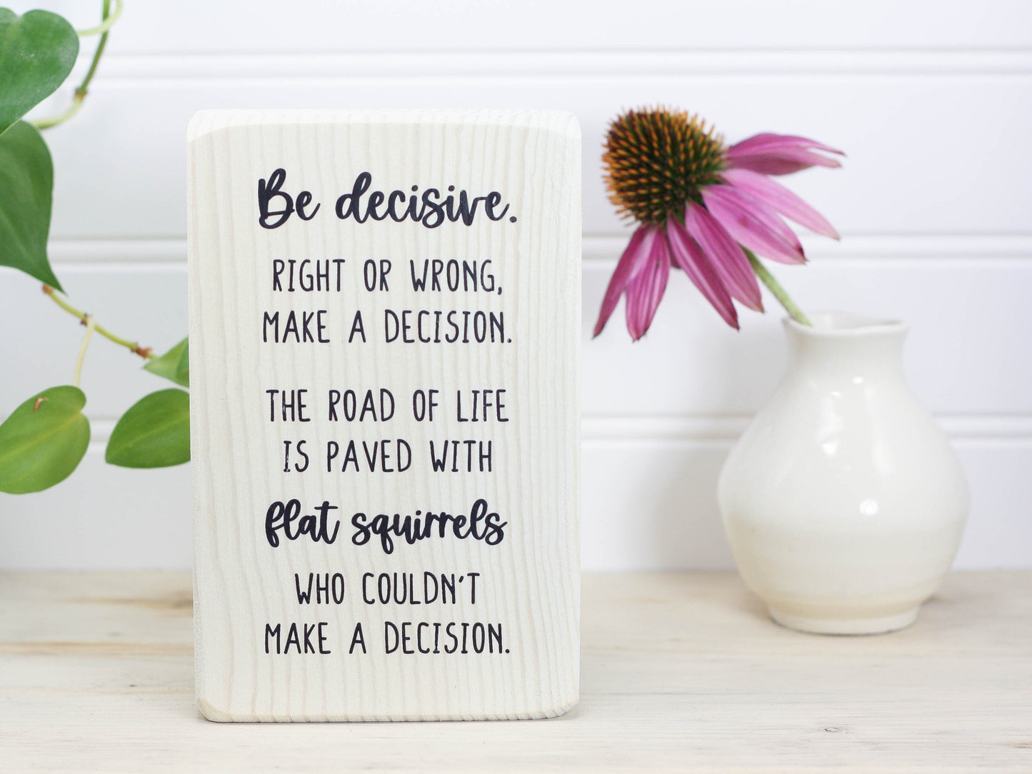 Small whitewashed wood freestanding sign in with the saying "Be decisive. Right or wrong, make a decision. The road of life is paved with flat squirrels who couldn't make a decision."