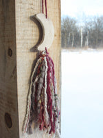 red, brown, cream tassel hanging from an off white wooden moon