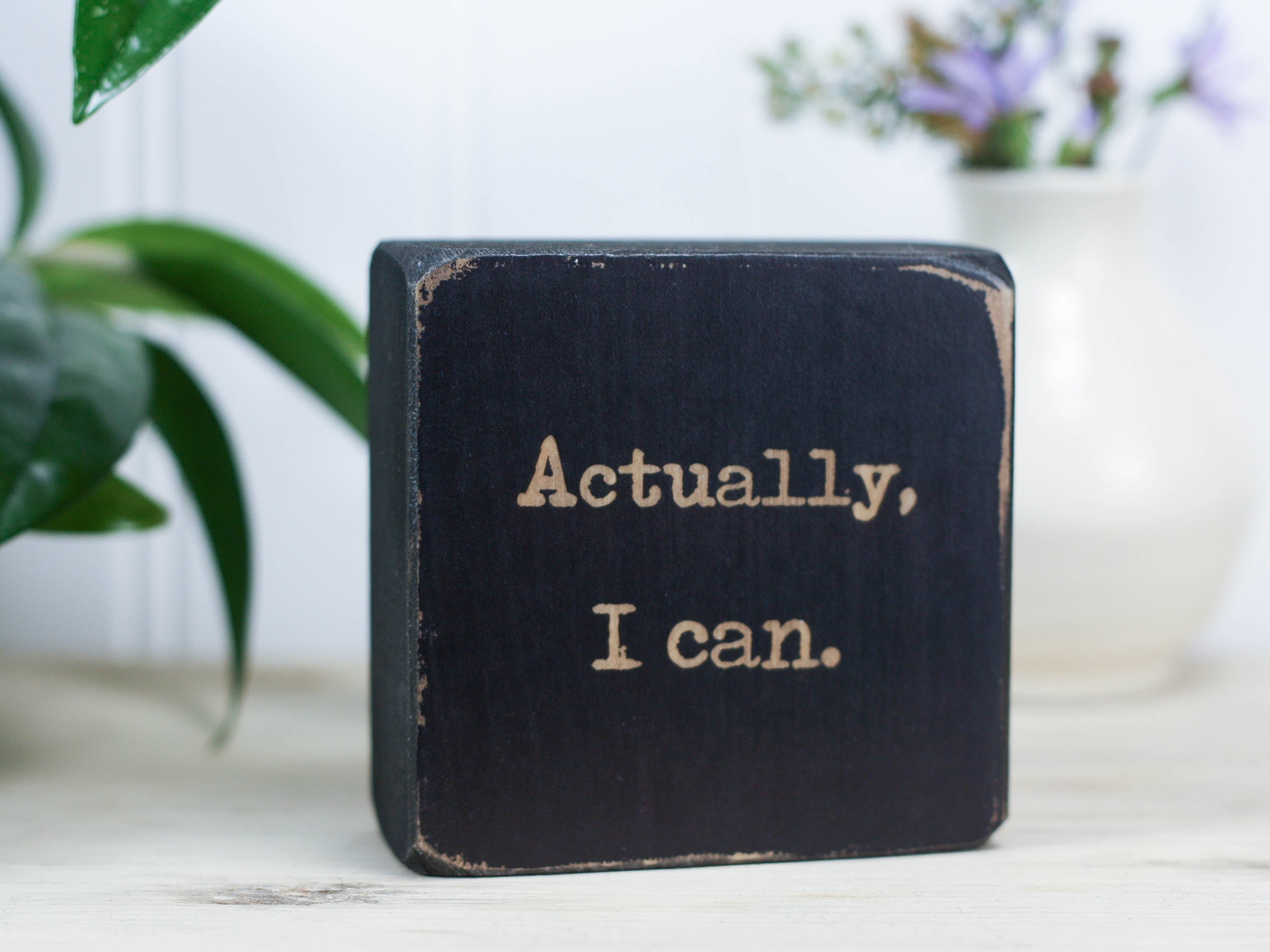 Small motivational wood sign in distressed black with the saying "Actually, I can."