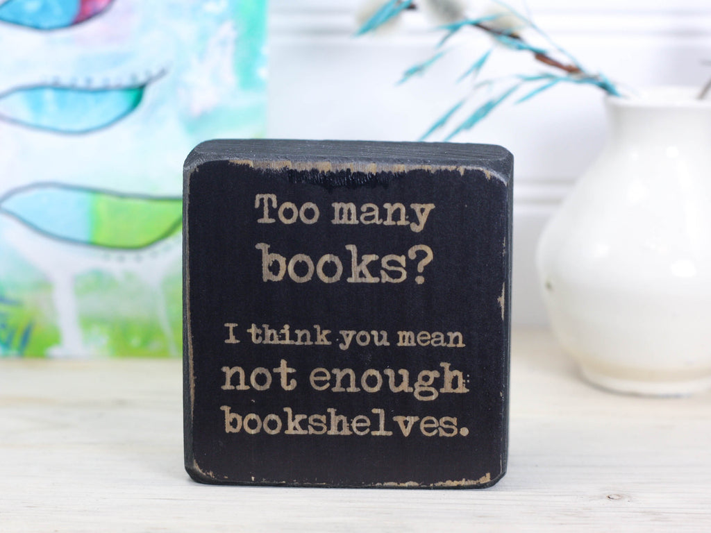 Small wood sign in distressed black with the saying "Too many books? I think you mean not enough bookshelves."