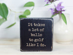 Small wooden sign in distressed black with the saying "It takes alot of balls to golf like I do."