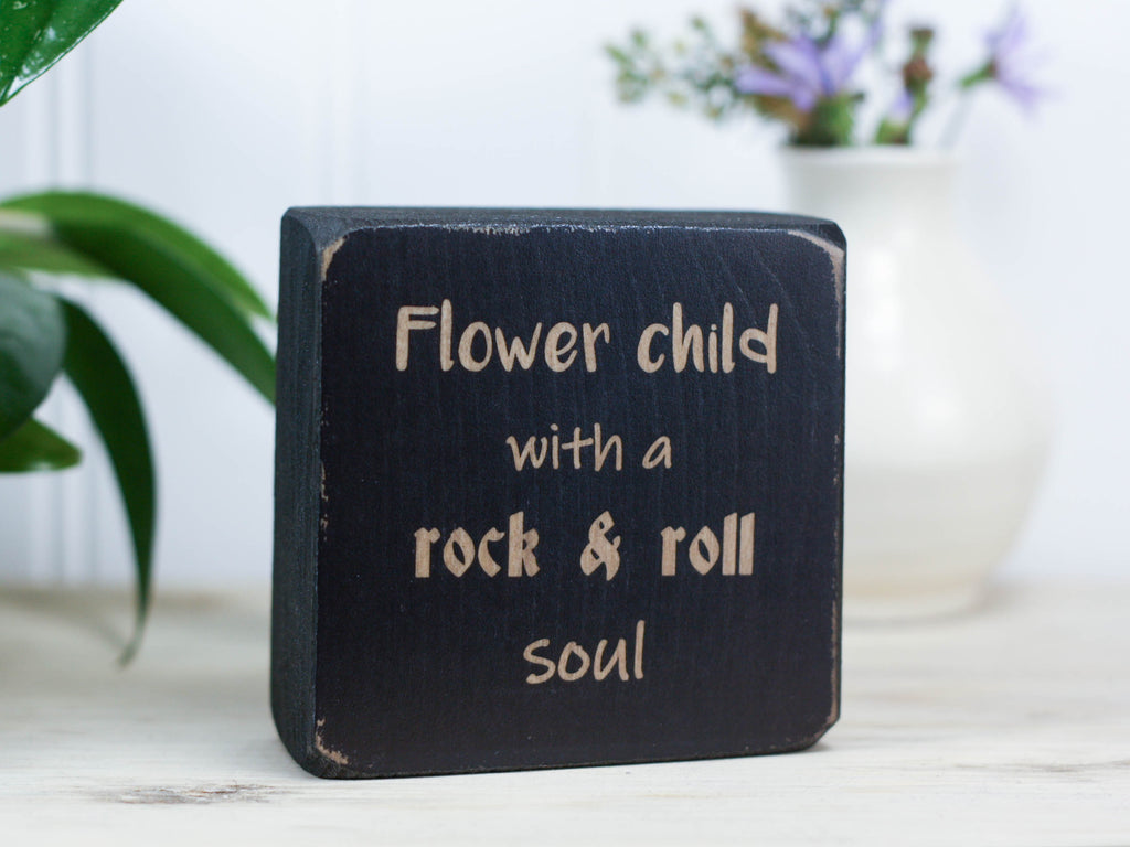 Small, freestanding, distressed black, solid wood sign with saying "Flower child with a rock & roll soul".