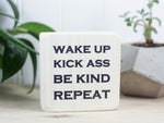 Small desk sign in whitewash with the saying "Wake up Kick ass Be kind Repeat".
