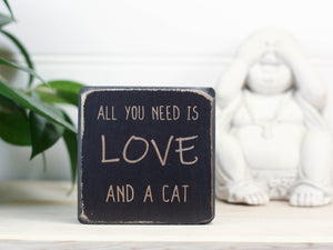 Small, freestanding, distressed black, solid wood sign with saying "All you need is love and a cat".