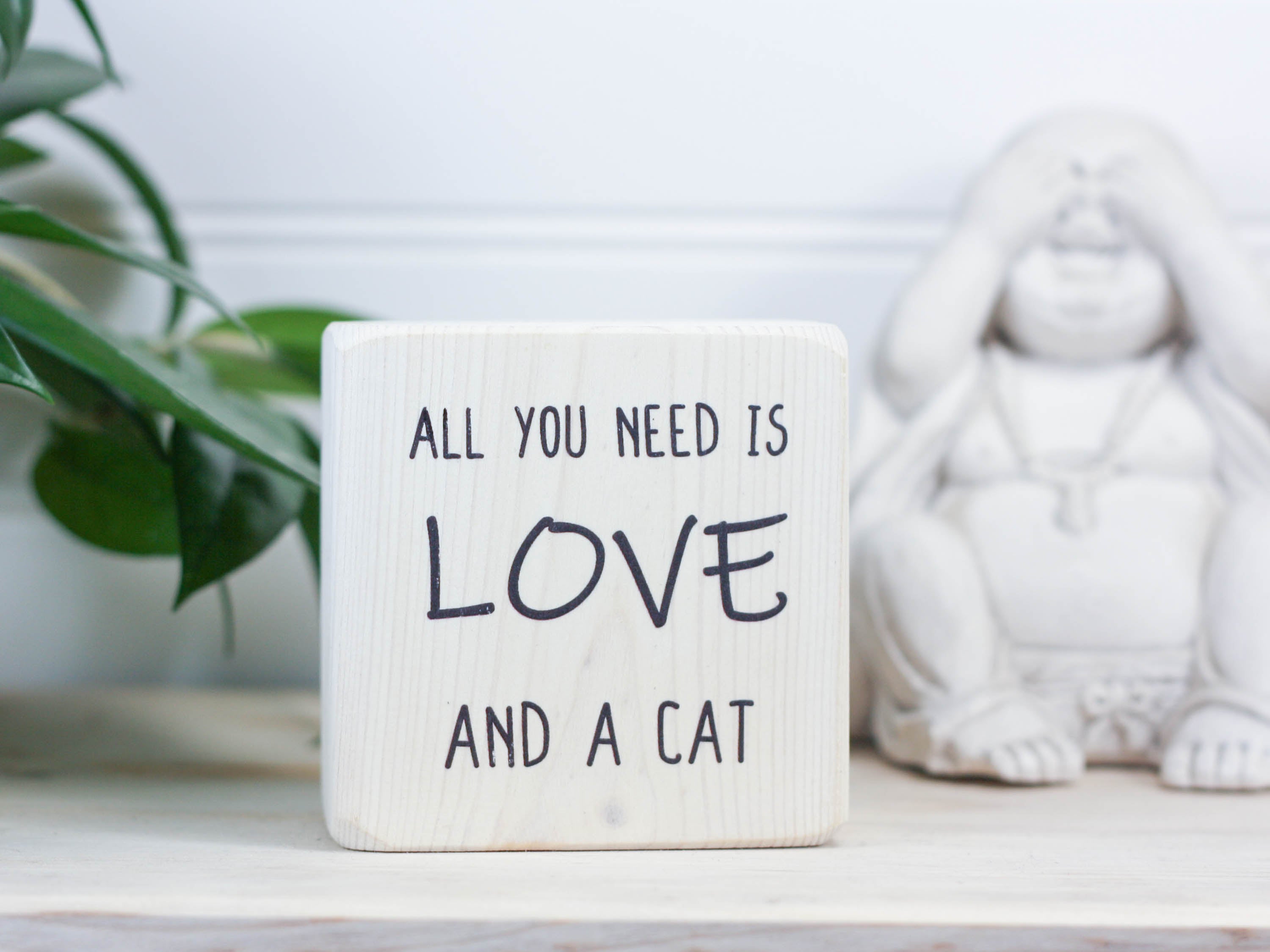 Small, freestanding, whitewash, solid wood sign with saying "All you need is love and a cat".