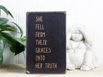 Small inspirational wood block sign in distressed black with the saying "She fell from their graces into her truth."