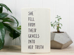 Small inspirational wood block sign in whitewash with the saying "She fell from their graces into her truth."