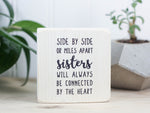 Small wood block with sister quote in whitewash that reads "Side by side or miles apart sisters will always be connected by the heart."