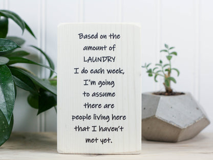 Small wood laundry sign in whitewash with the saying "Based on the amount of laundry I do each week, I'm going to assume there are people living here that I haven't met yet."