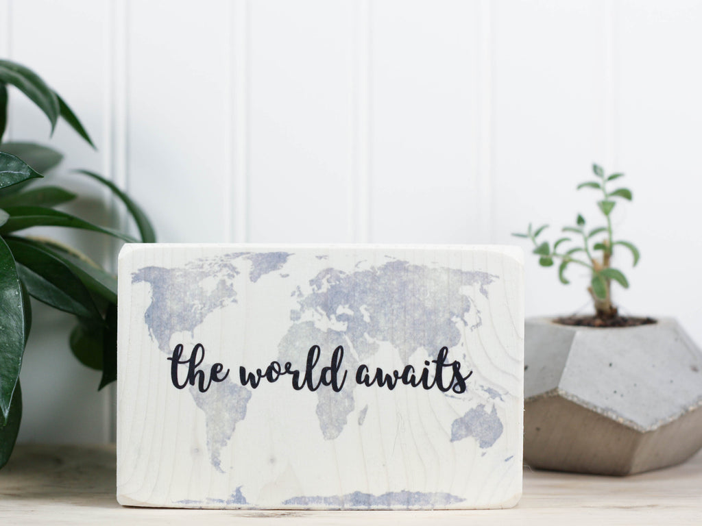 Small wood quote block in whitewash with the saying "The world awaits".