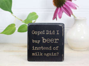 Mini wood sign in distressed black with the saying "Oops! Did I buy beer instead of milk...again?"