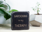 Small, freestanding, distressed black, solid wood sign with saying "Gardening is my therapy".