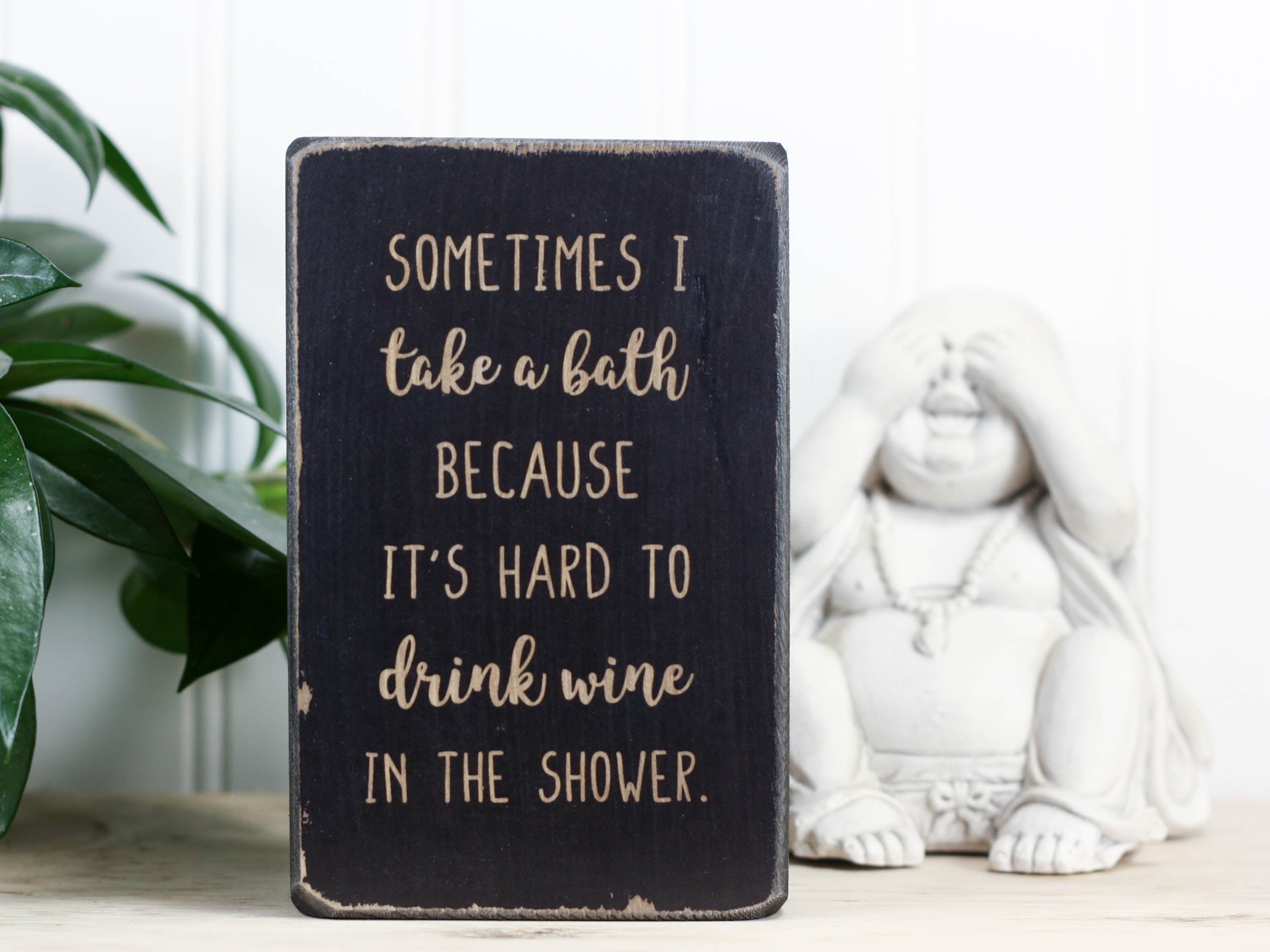 Small wood sign in distressed black with the saying "Sometimes I take a bath because it's hard to drink wine in the shower."
