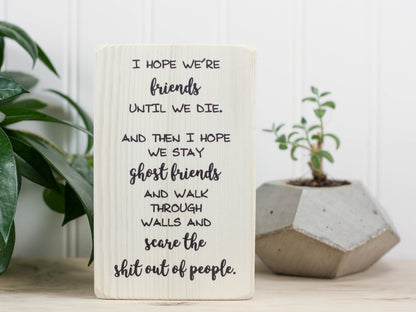 Small wood sign in whitewash with the saying "I hope we're friends until we die. And then I hope we stay ghost friends and walk through walls and scare the shit out of people."