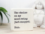 Small wood sign in whitewash with the saying "The chains on my mood swing just snapped. Run."