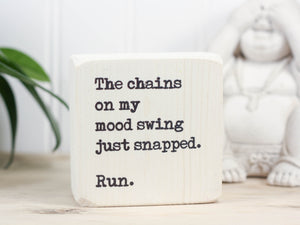 Small wood sign in whitewash with the saying "The chains on my mood swing just snapped. Run."