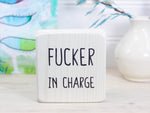Small whitewash freestanding wood sign with the text "fucker in charge"