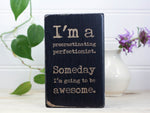 Small wood sign in distressed black with the saying "I'm a procrastinating perfectionist. Someday I'm going to be awesome."