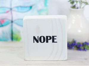 Small freestanding wood sign in whitewash with the word "nope"