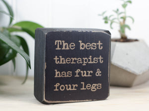 Small wood sign in distressed black with the saying "The best therapist has fur and four legs".
