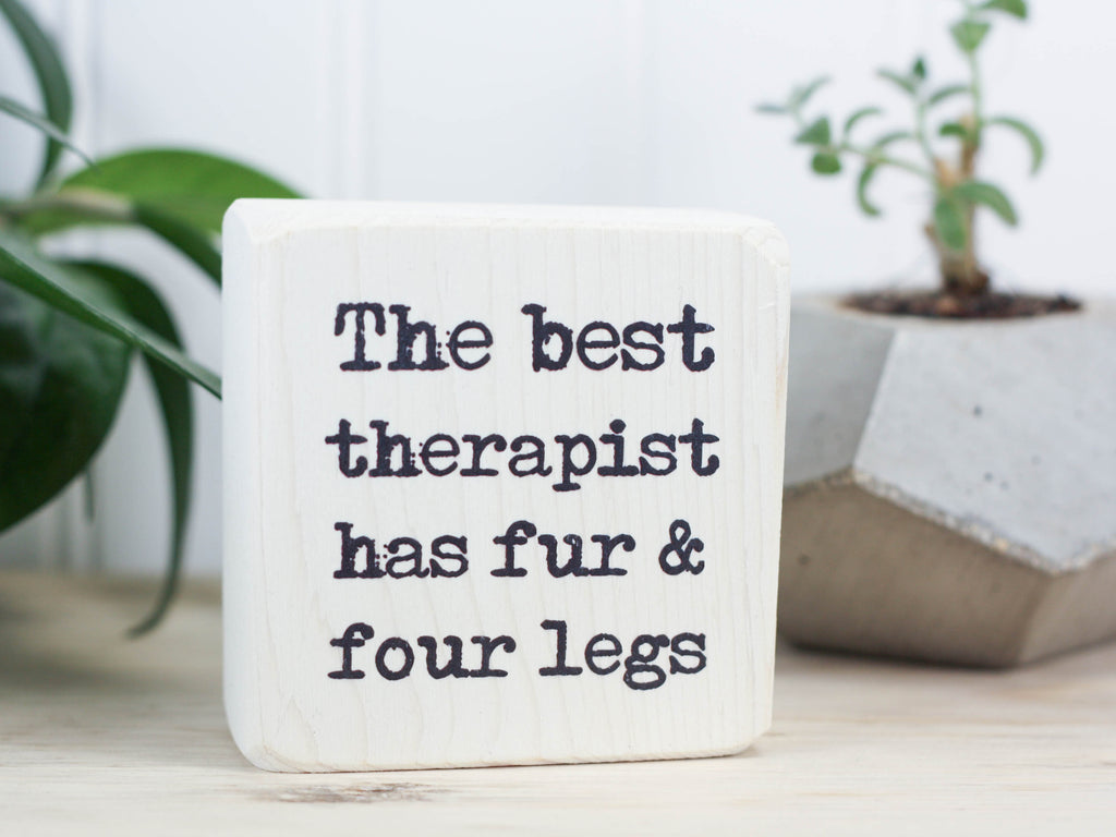 Small wood sign in whitewash with the saying "The best therapist has fur and four legs".