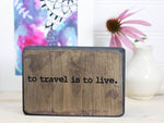 Small wood travel sign in distressed black with the saying "To travel is to live".