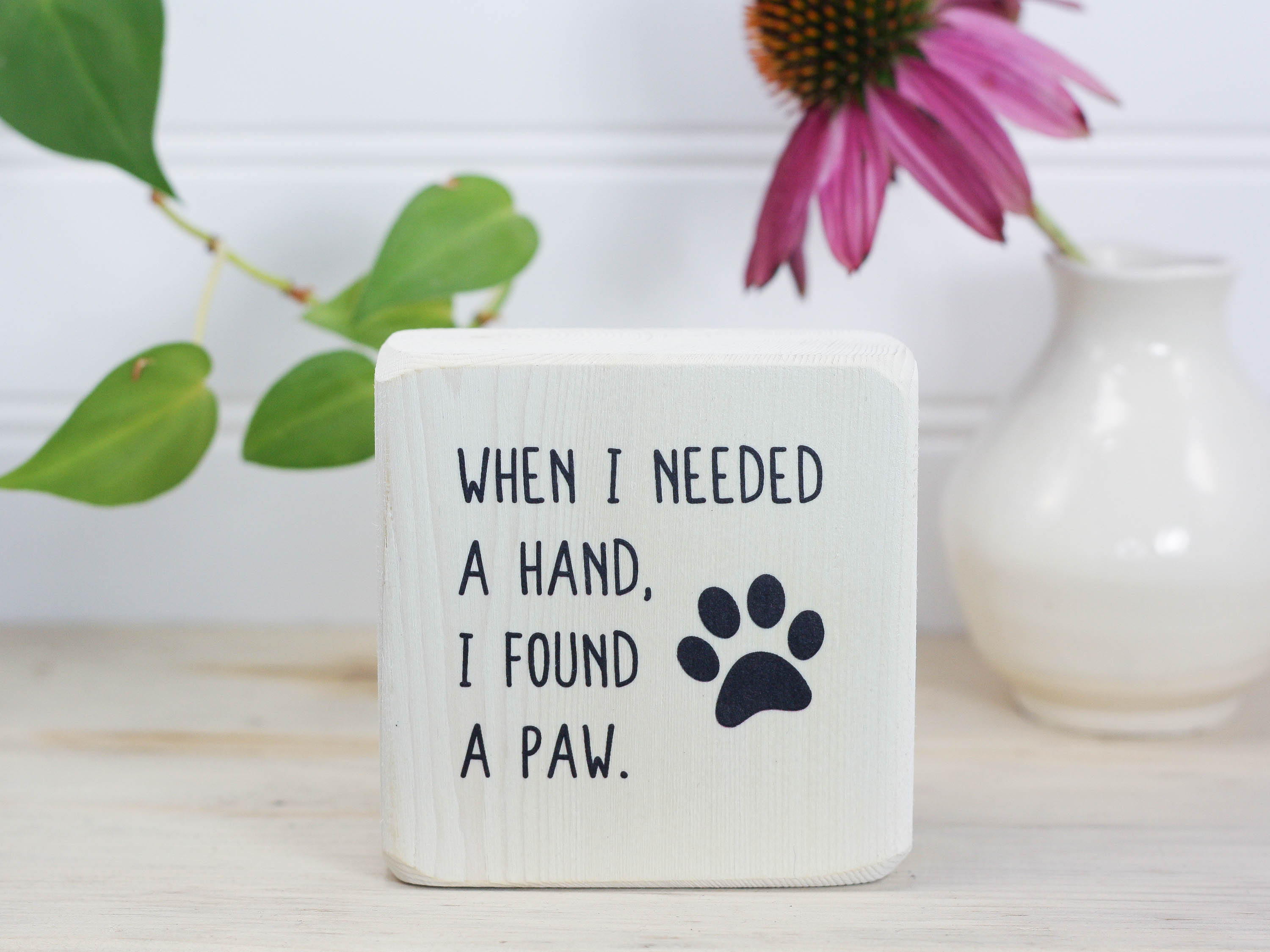 Small wood sign in whitewash with the saying "When I needed a hand, I found a paw".