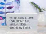 Small free-standing wood sign in whitewash with the saying "When life hands me lemons I make chocolate cake, and leave bitches wondering how I did it.
