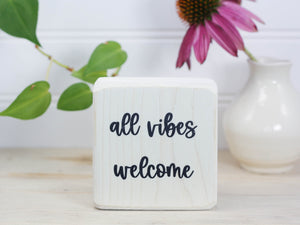 Small wood sign in whitewash with the saying "all vibes welcome"