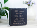 Small, freestanding, distressed black, solid wood sign with a funny saying on it "I smile because you're my brother. I laugh because there's nothing you can do about it."
