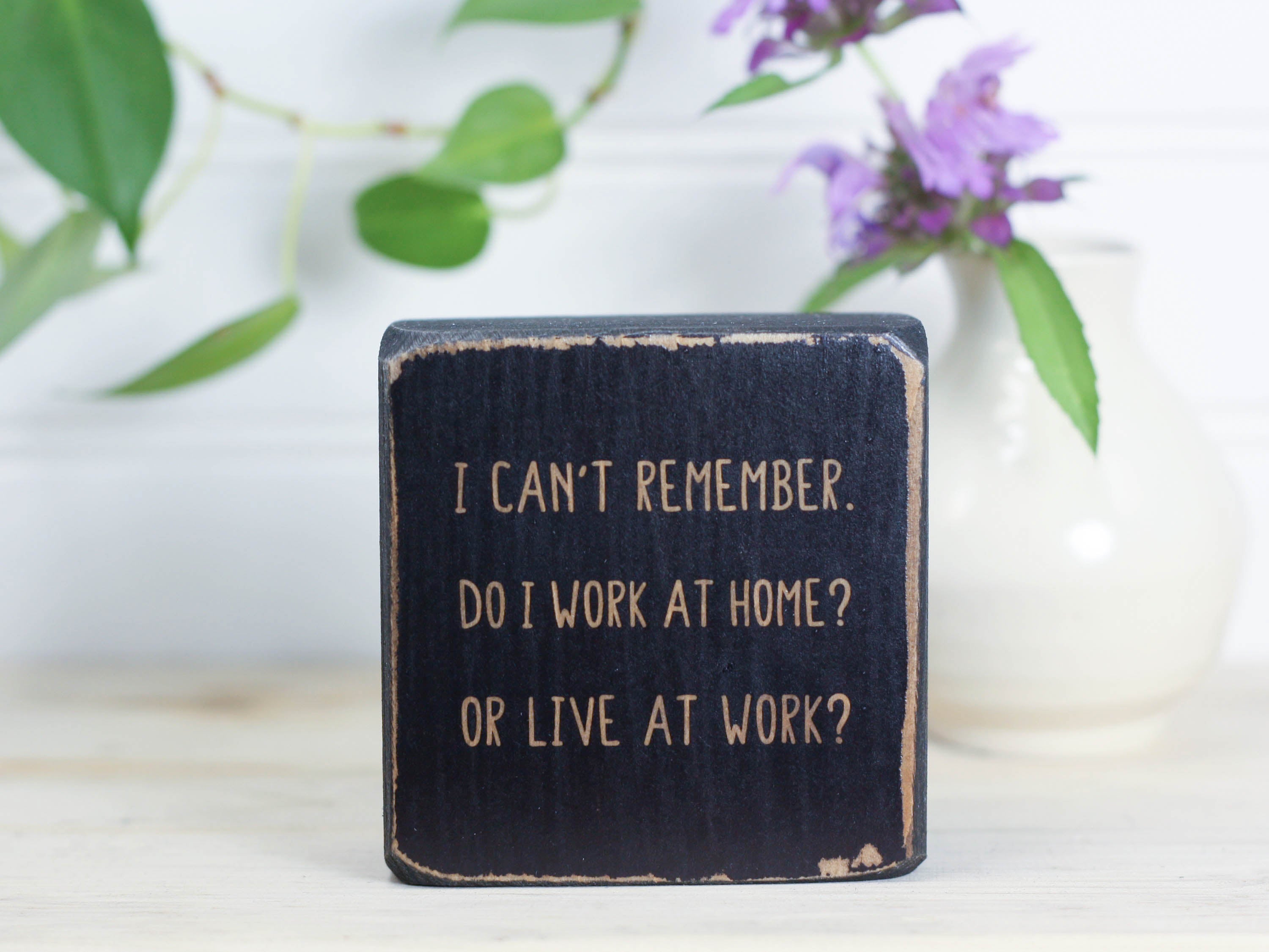 Small, freestanding distressed black wood sign with a funny saying on it "I can't remember. Do I work at home? Or live at work?"