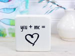 Mini wood shelf sign in whitewash with the text "you + me = (heart image)"