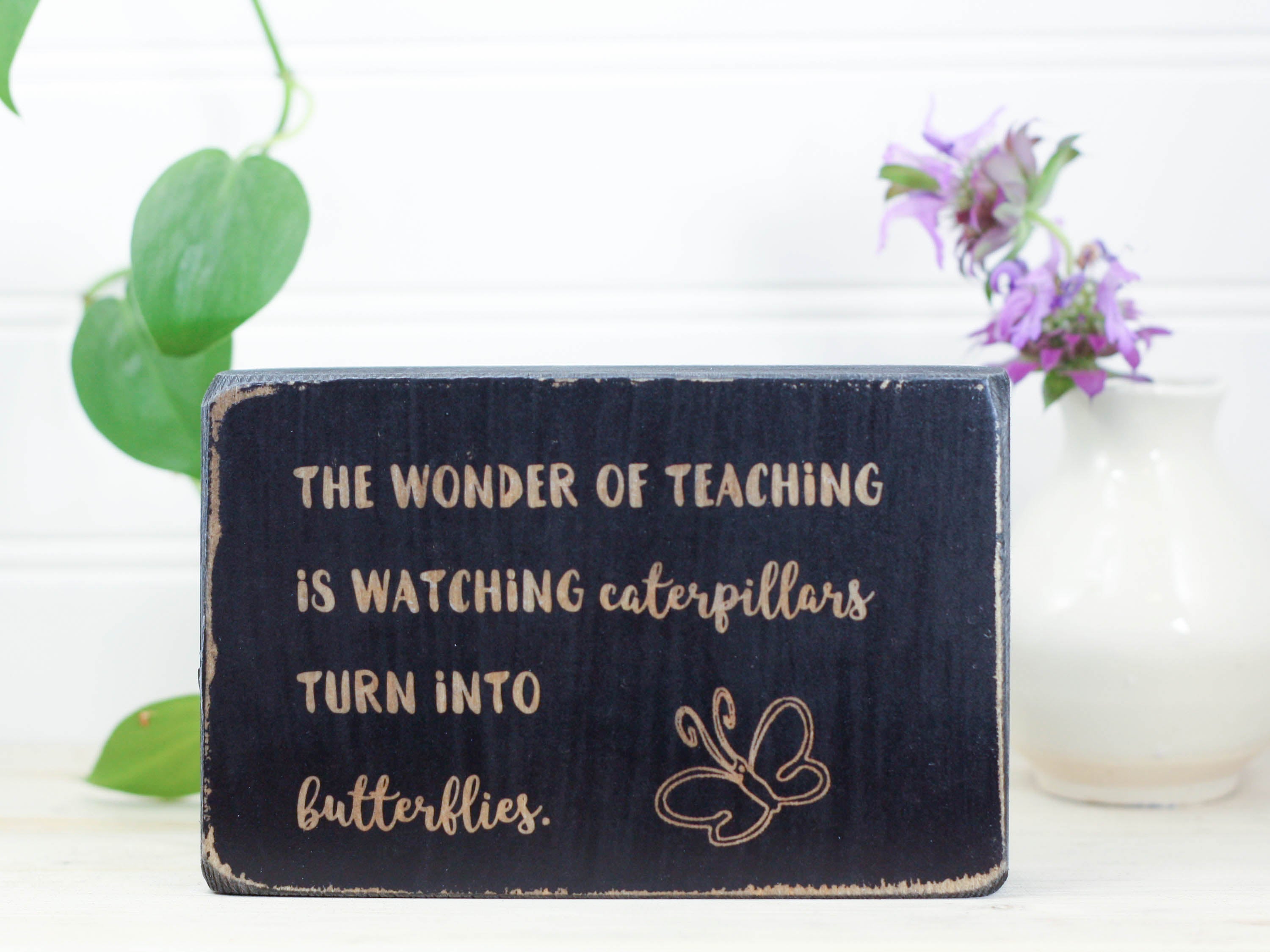 Small wood teacher gift in distressed black with the saying "The wonder of teaching is watching caterpillars turn into butterflies."