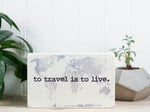 Small wood travel sign in whitewash with the saying "To travel is to live".