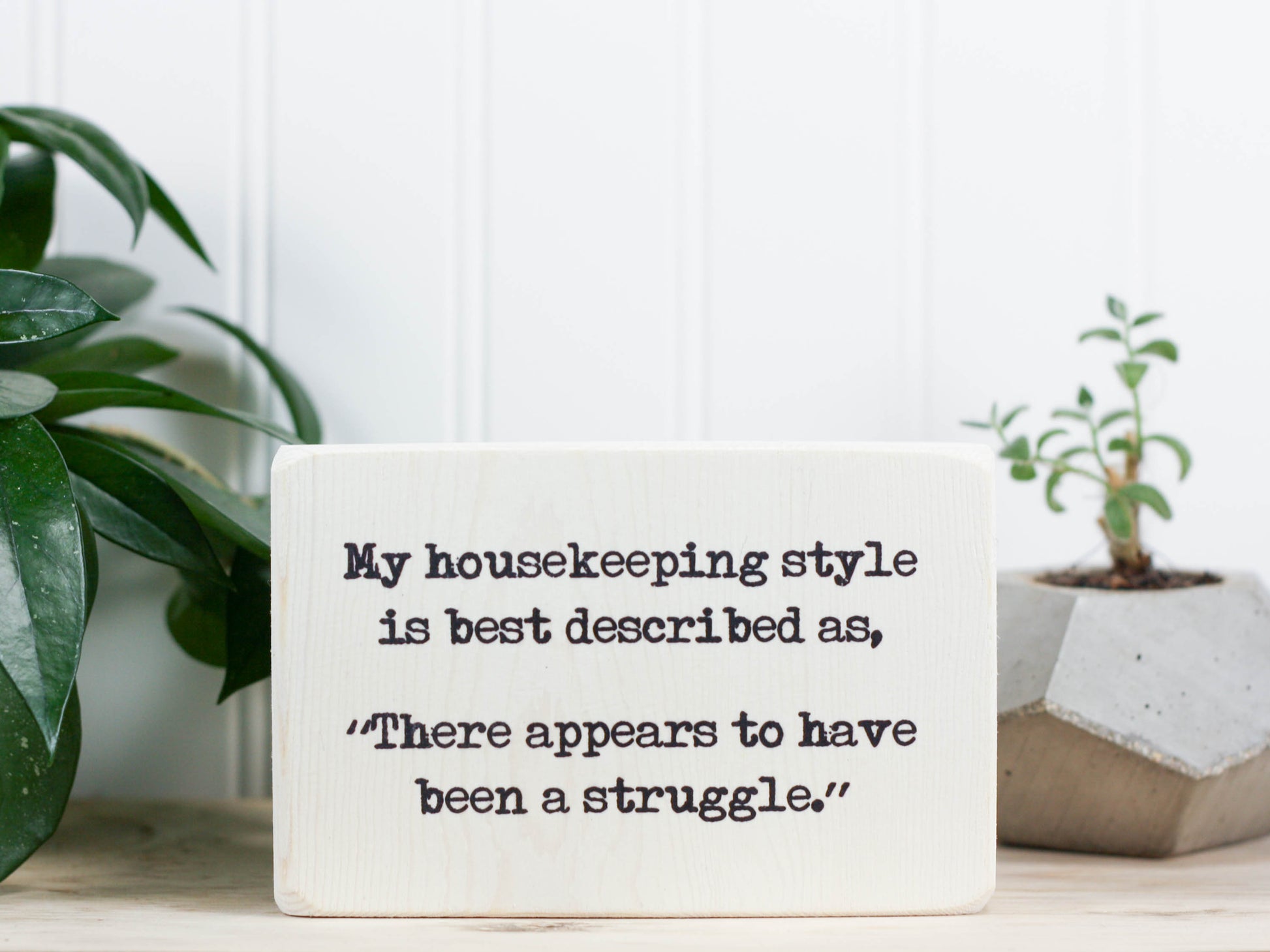 Small funny wood sign in whitewash with the saying "My housekeeping style is best desribed as, "There appears to have been a struggle."