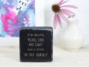 Small funny wood sign in distressed black with the saying "I'm mostly peace, love and light and a little go fuck yourself".