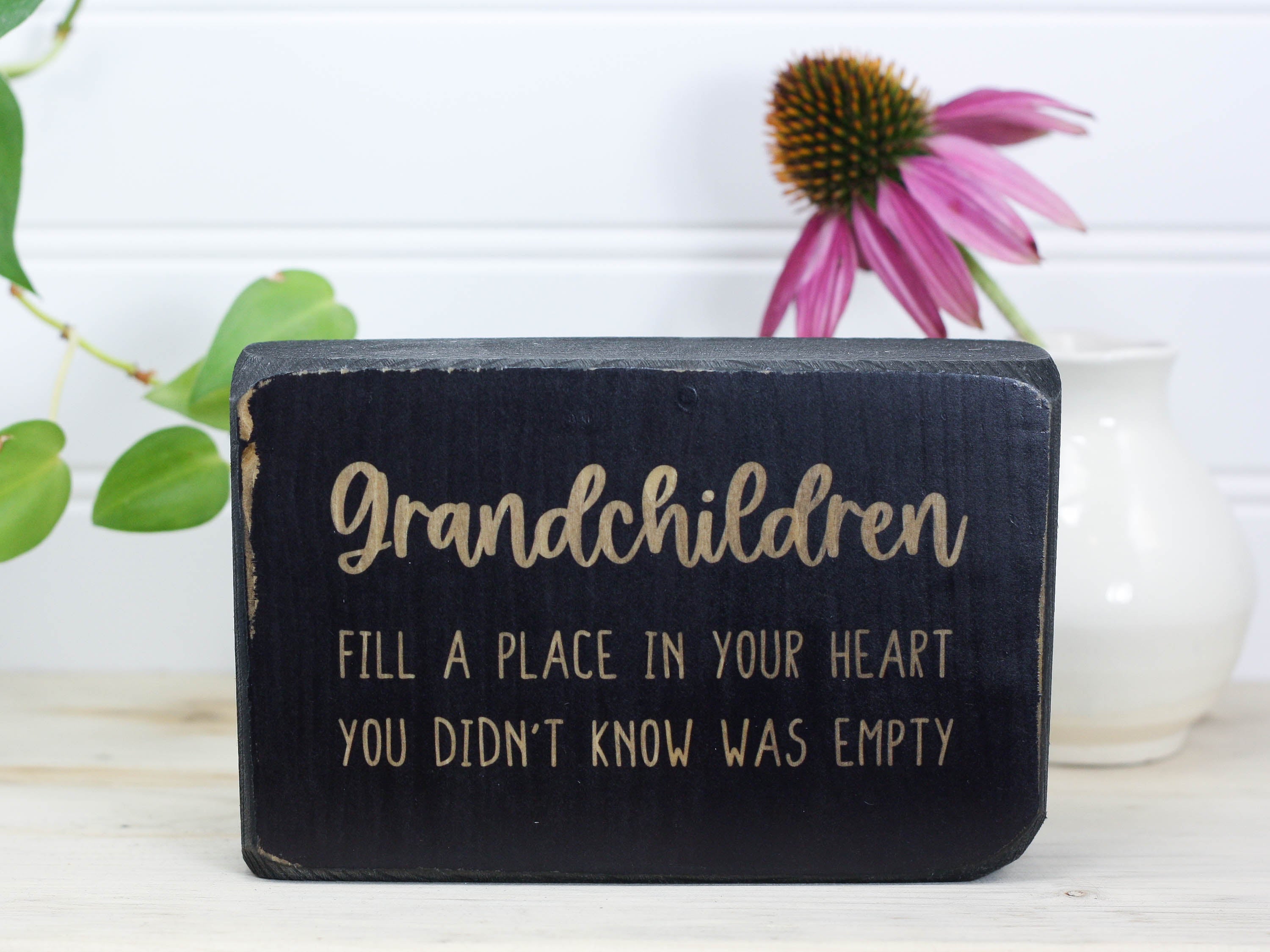 Small distressed black wooden sign with the saying "Grandchildren fill a place in your heart you didn't know was empty. "