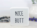 Small wood sign in whitewash with the text "nice butt" on it