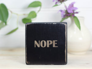 Small freestanding wood sign in distressed black with the word "nope"