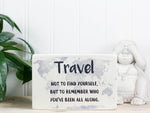 Small wood travel sign in whitewash with the saying "Travel not to find yourself, but to remember who you've been all along."