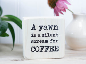 Funny kitchen sign in whitewash with the saying "A yawn is a silent scream for coffee".