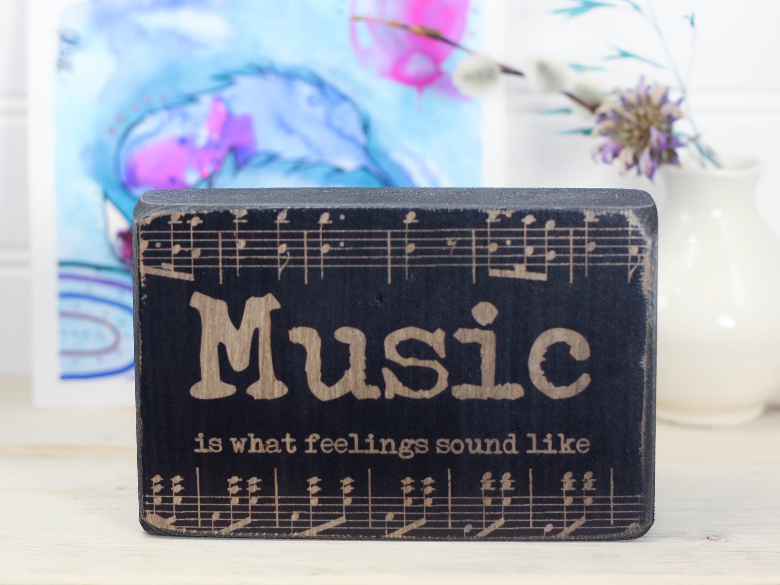 Small wood sign in distressed black with music notes and the saying "Music is what feelings sound like".