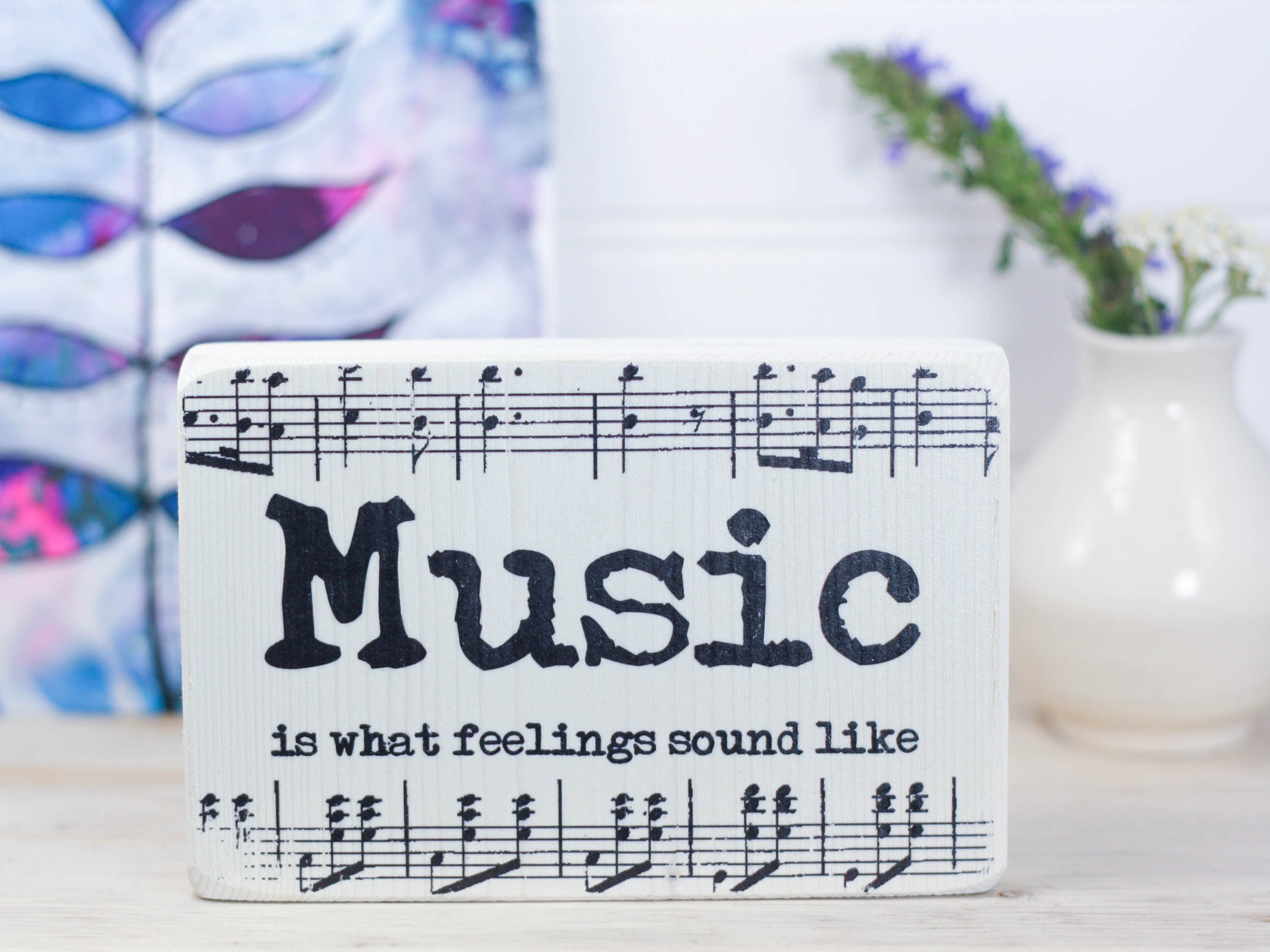 Small wood sign in whitewash with music notes and the saying "Music is what feelings sound like".
